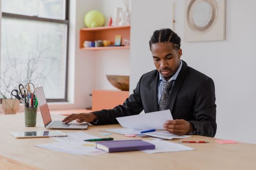 Free A professional businessman in a suit working at a desk with documents and a laptop in an office setting. Stock Photo
