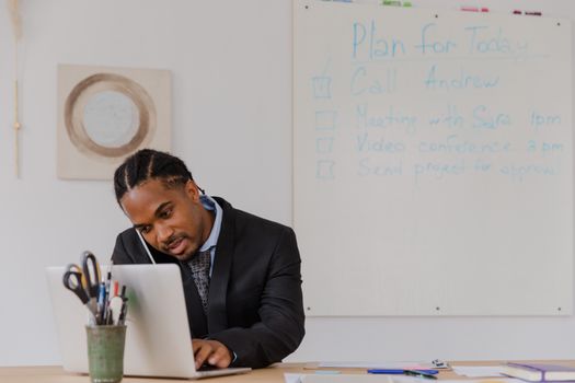 Businessman at his desk in an office working on a laptop and making phone calls.