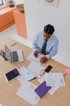 Businessman in a modern office reviewing documents and working on a laptop from a top view.