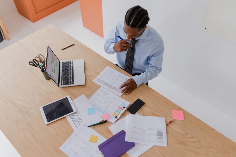Professional businessman analyzing documents at a desk, working indoors with a laptop and tablet.