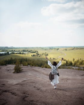 A woman with a backpack walks freely toward a vast, green landscape under a bright sky.