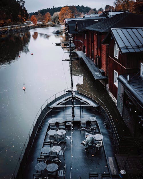 Man Sitting on Boat Deck Docked Beside Houses on River