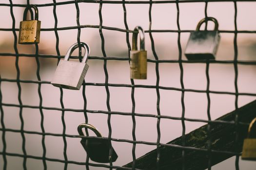 Close-up of romantic love padlocks hanging on a metal wire mesh fence by a river.