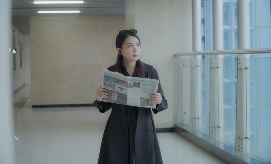 大人の女性がコートを着て、モダンな室内の環境で新聞を読んでいます。