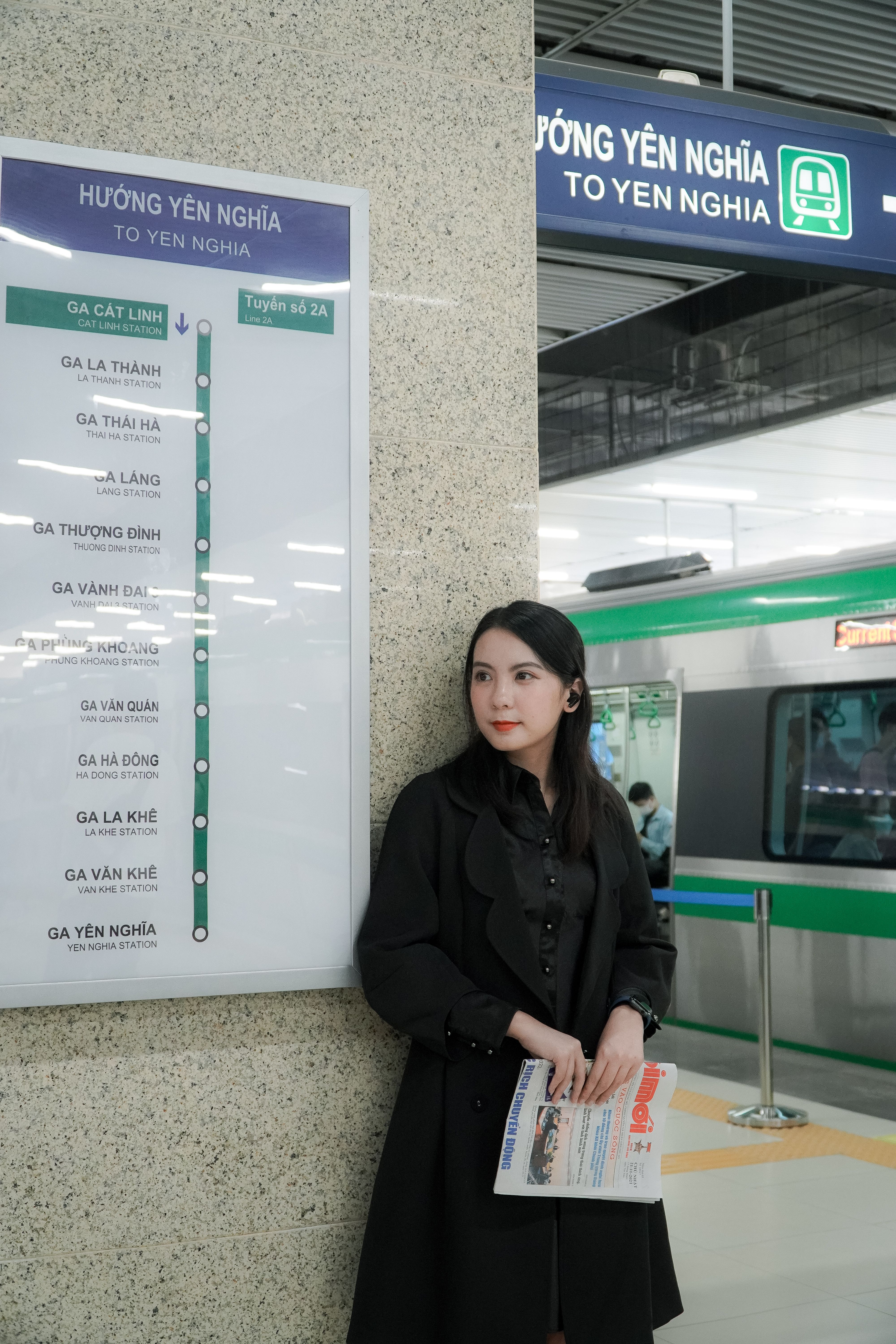 Asian woman standing at Yen Nghia Metro Station with a train on the platform.