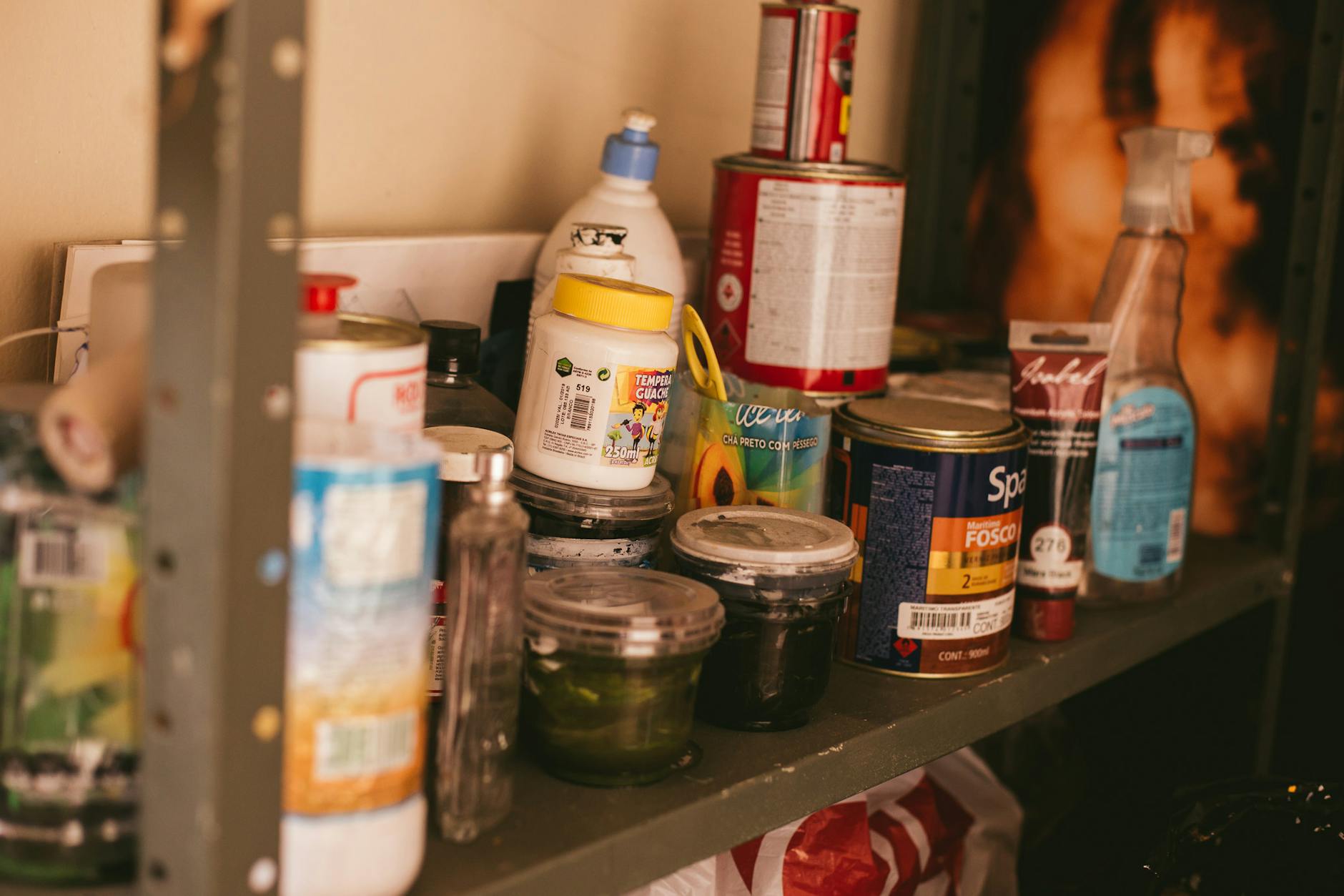 A cluttered shelf in a workshop stocked with various paint containers and supplies.