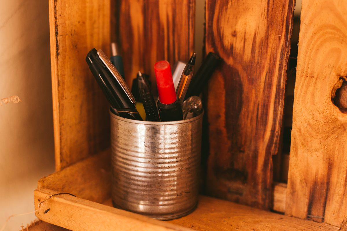 A vintage tin can reused as a pencil holder on a rustic wooden shelf