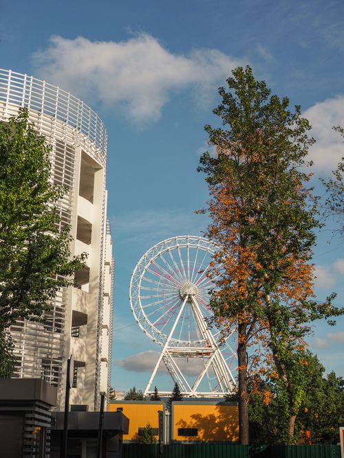 Free City scene with ferris wheel, trees, and building under a blue sky. Stock Photo