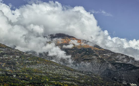 A scenic view of cloud-covered mountains in Aoste, Italy with vibrant autumnal colors.