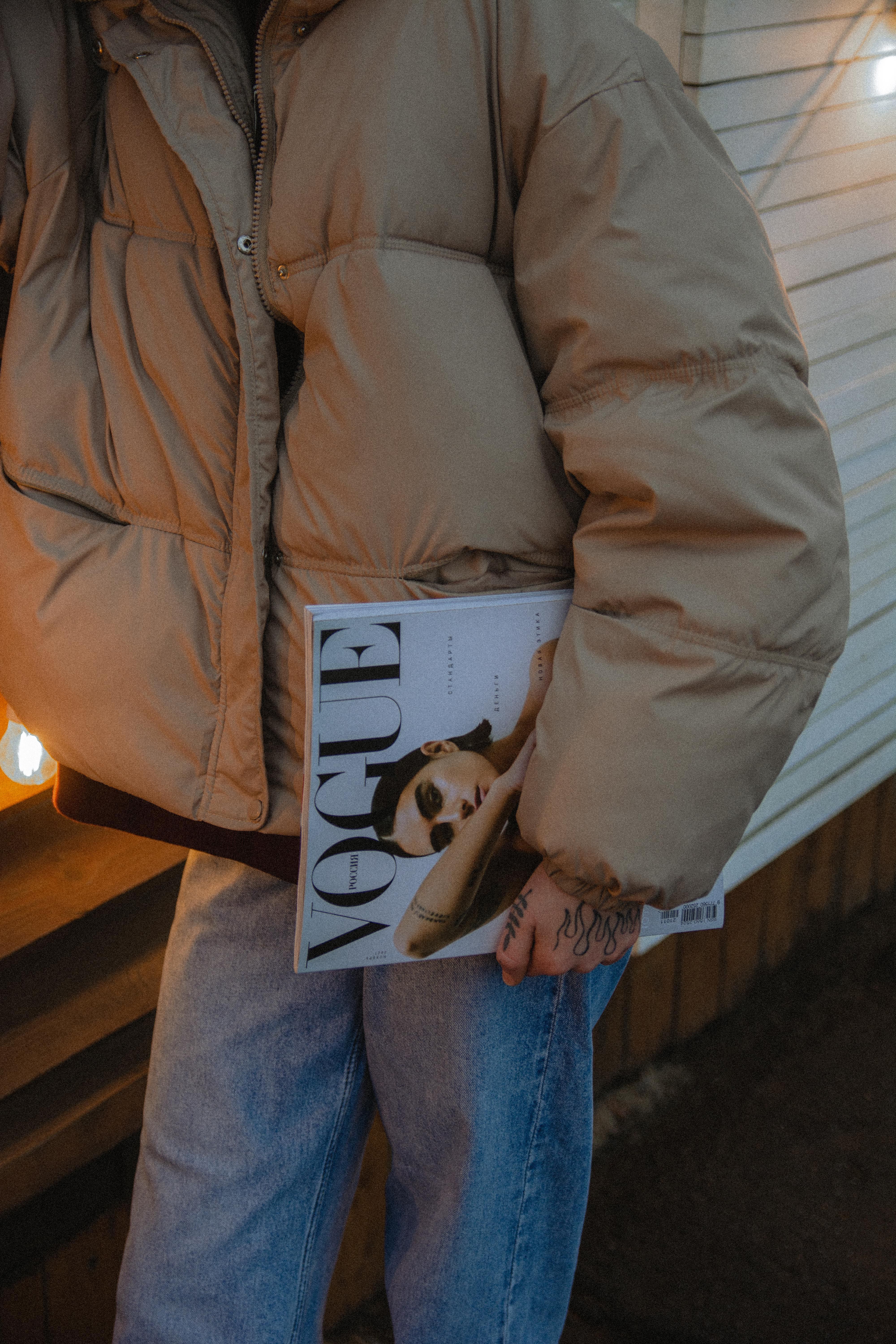 Stylish individual in denim jeans holding Vogue magazine against a winter backdrop.