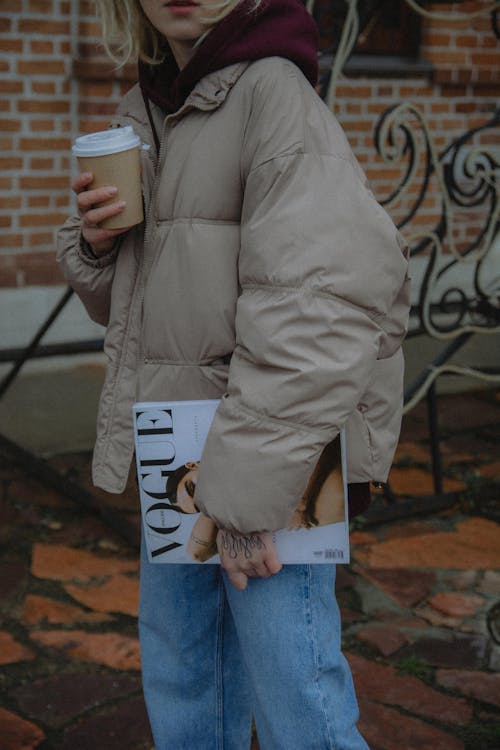 A Person in Brown Jacket Holding a Cup and a Magazine