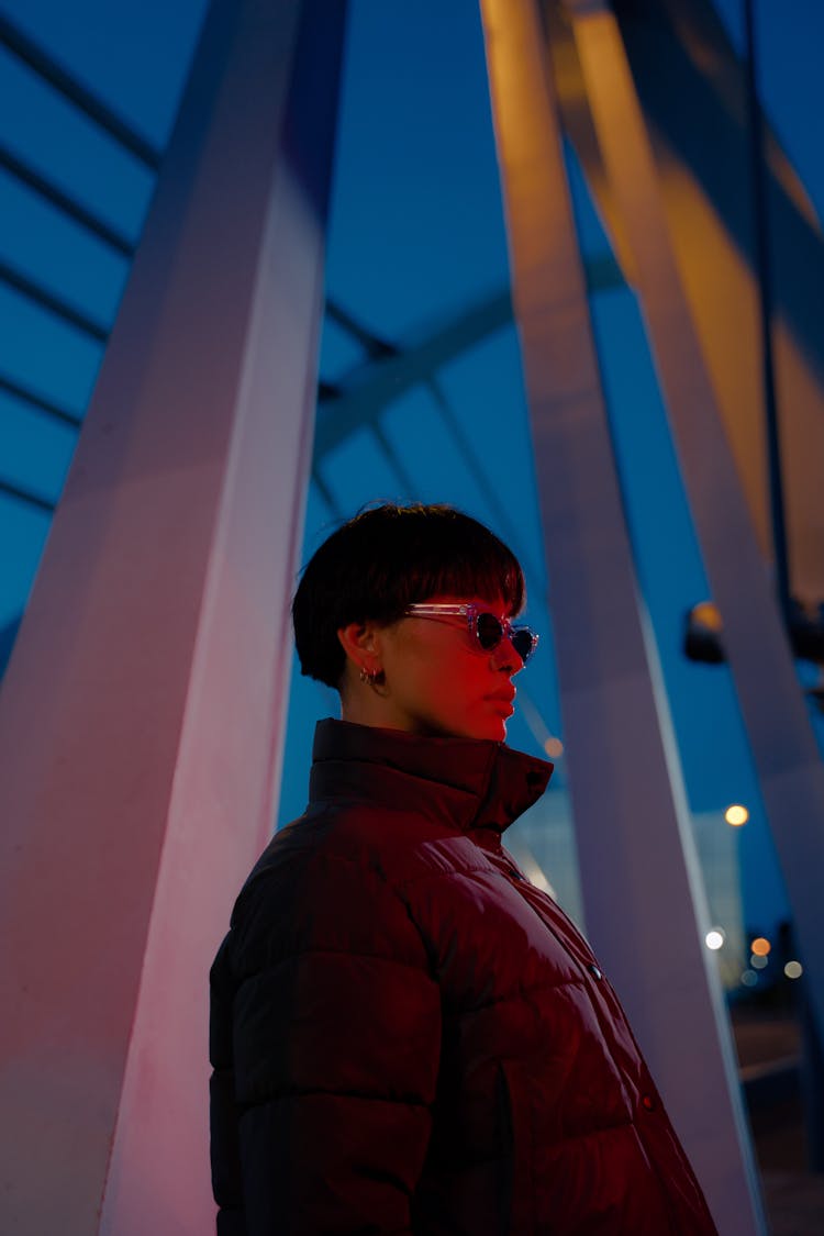 A Woman In Black Jacket Wearing Sunglasses Standing Beside A Steel Column