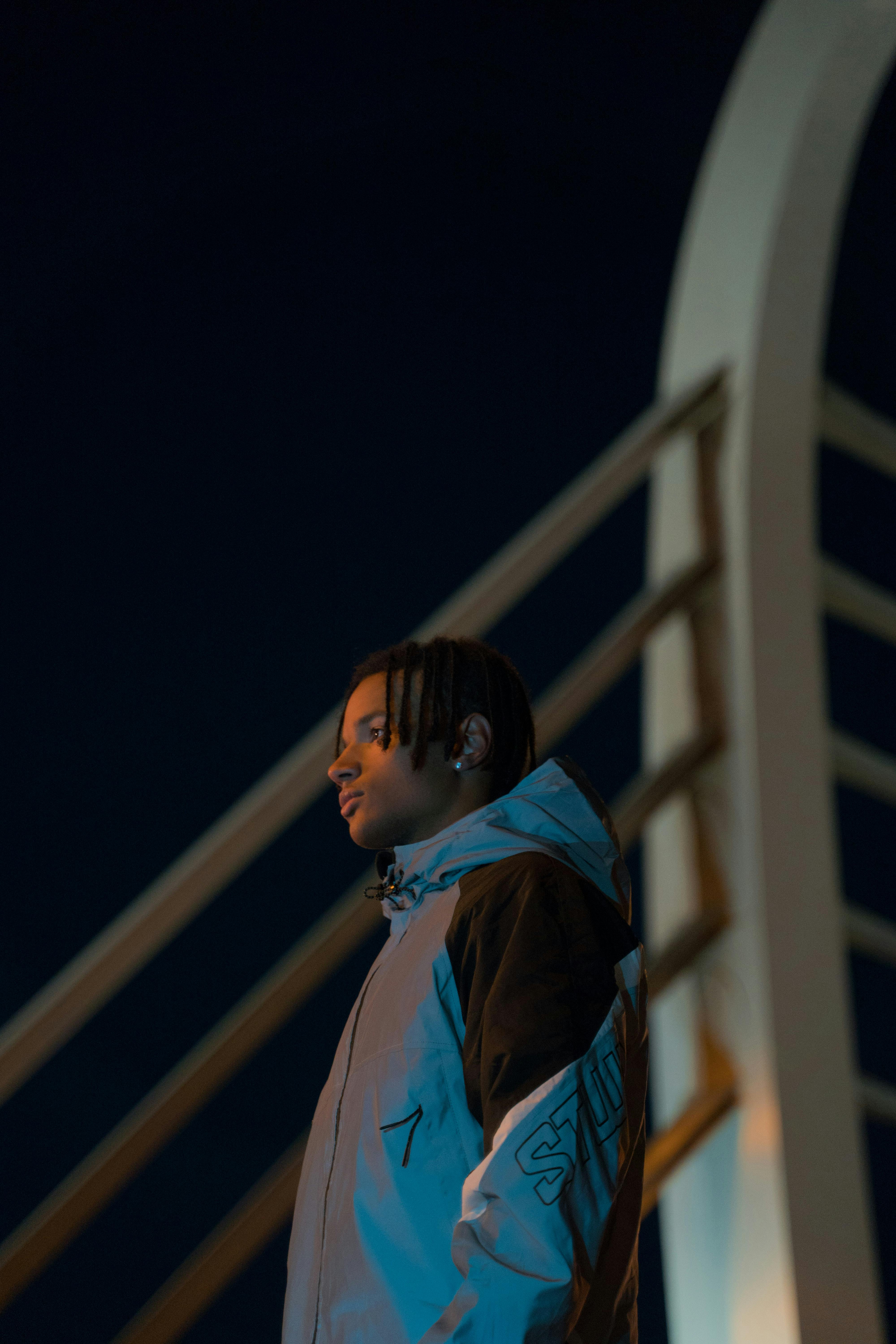 a man wearing gray and black jacket standing on a bridge