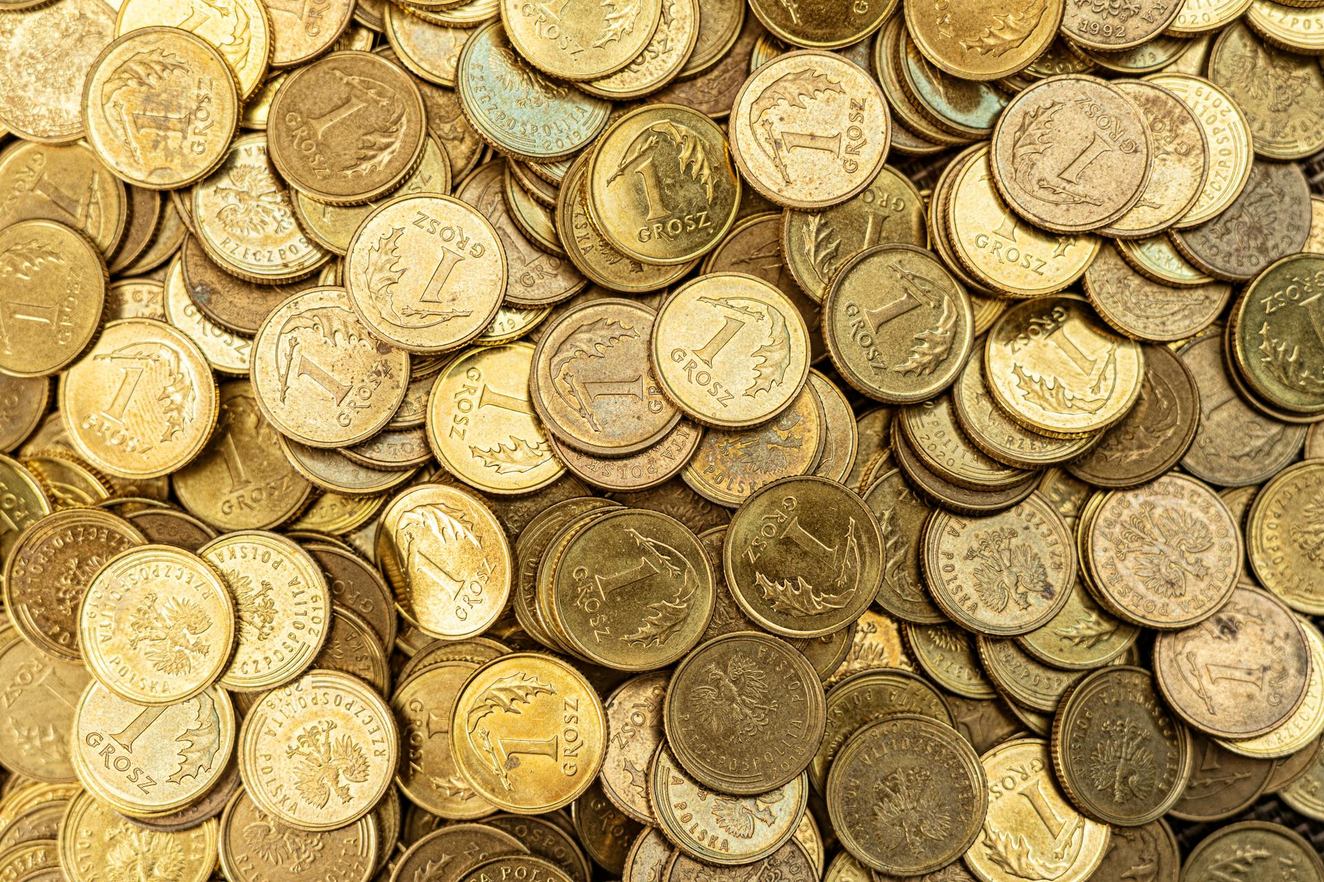 Close-up photograph of numerous Polish grosz coins arranged chaotically.