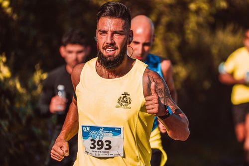 Free A focused male runner in a yellow jersey participates in an outdoor marathon with a thumbs-up gesture. Stock Photo