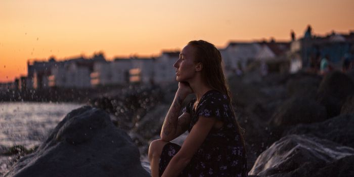 A woman sits by the sea at sunset, contemplating life. The water drops create a serene mood.