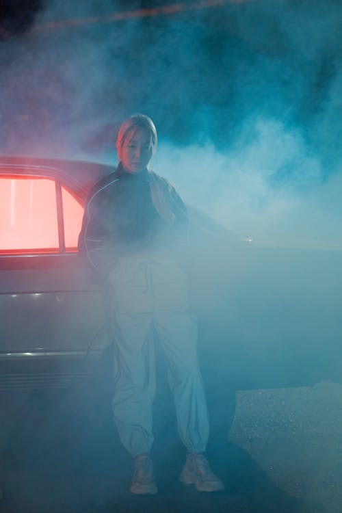 Free A Woman Standing Beside an Automobile Surrounded by Smoke Stock Photo