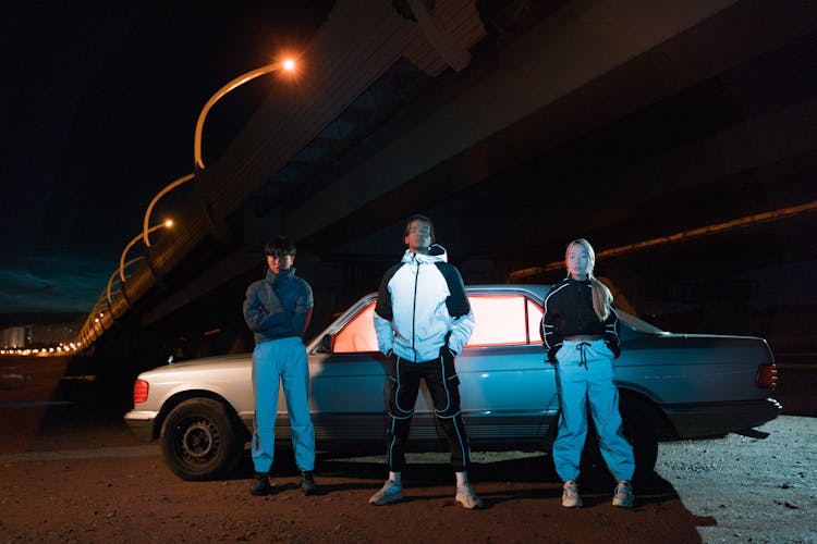 People Standing Beside The Car Parked Under A Bridge