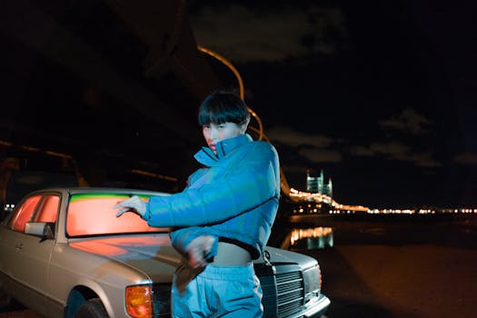 Asian woman with short hair in puffer jacket by vintage car at night.