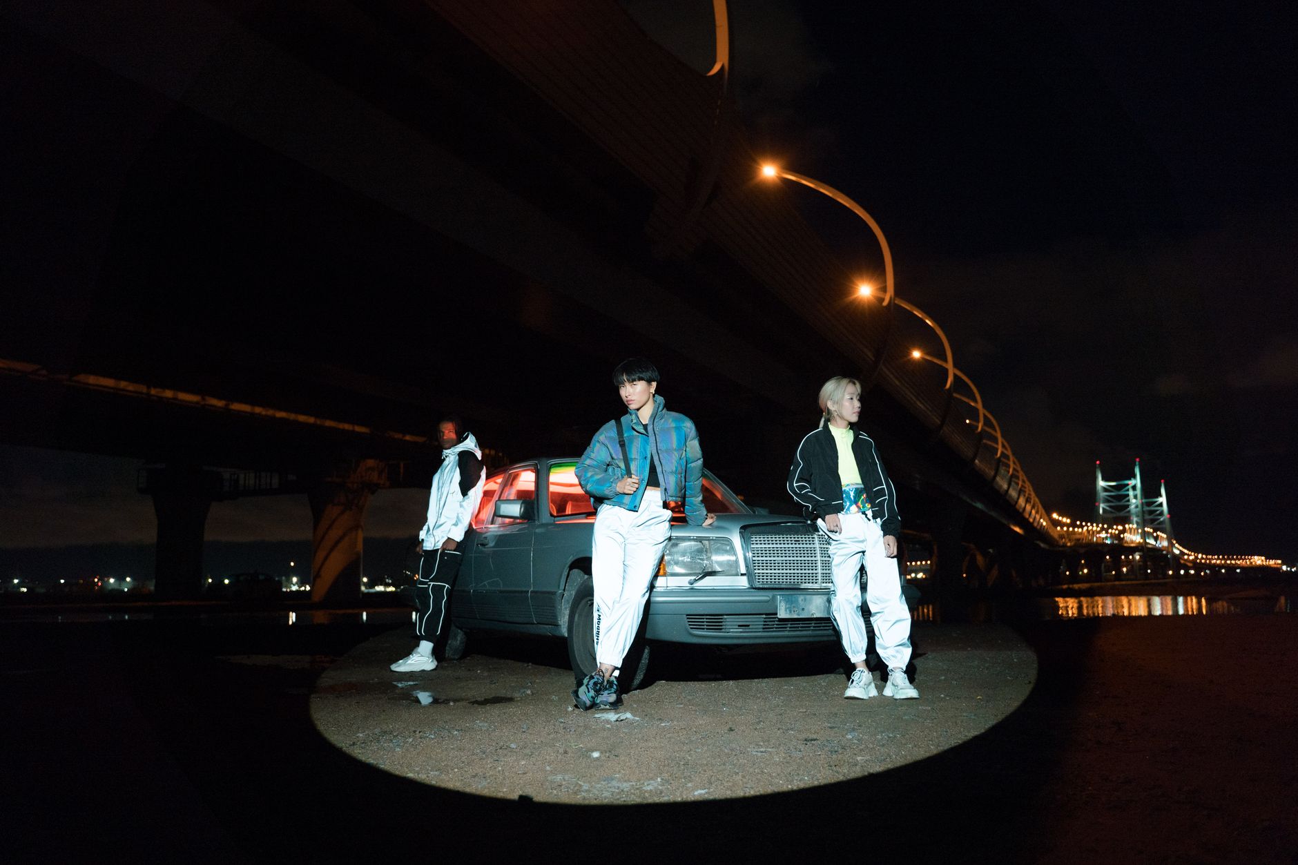 Stylish group posing with car under illuminated bridge during night.
