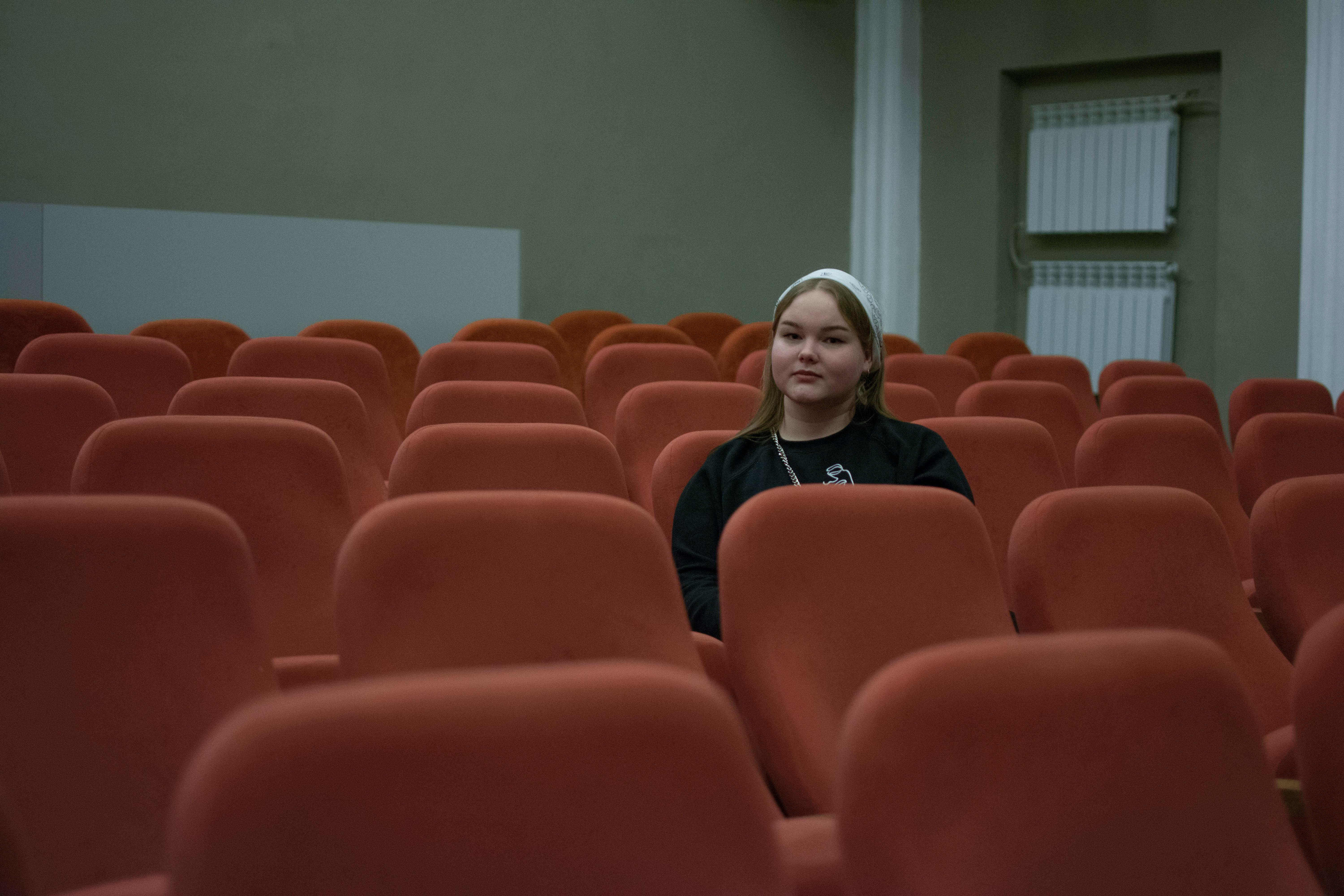 Free A woman sits alone in a theater with rows of red seats around her, creating a serene atmosphere. Stock Photo