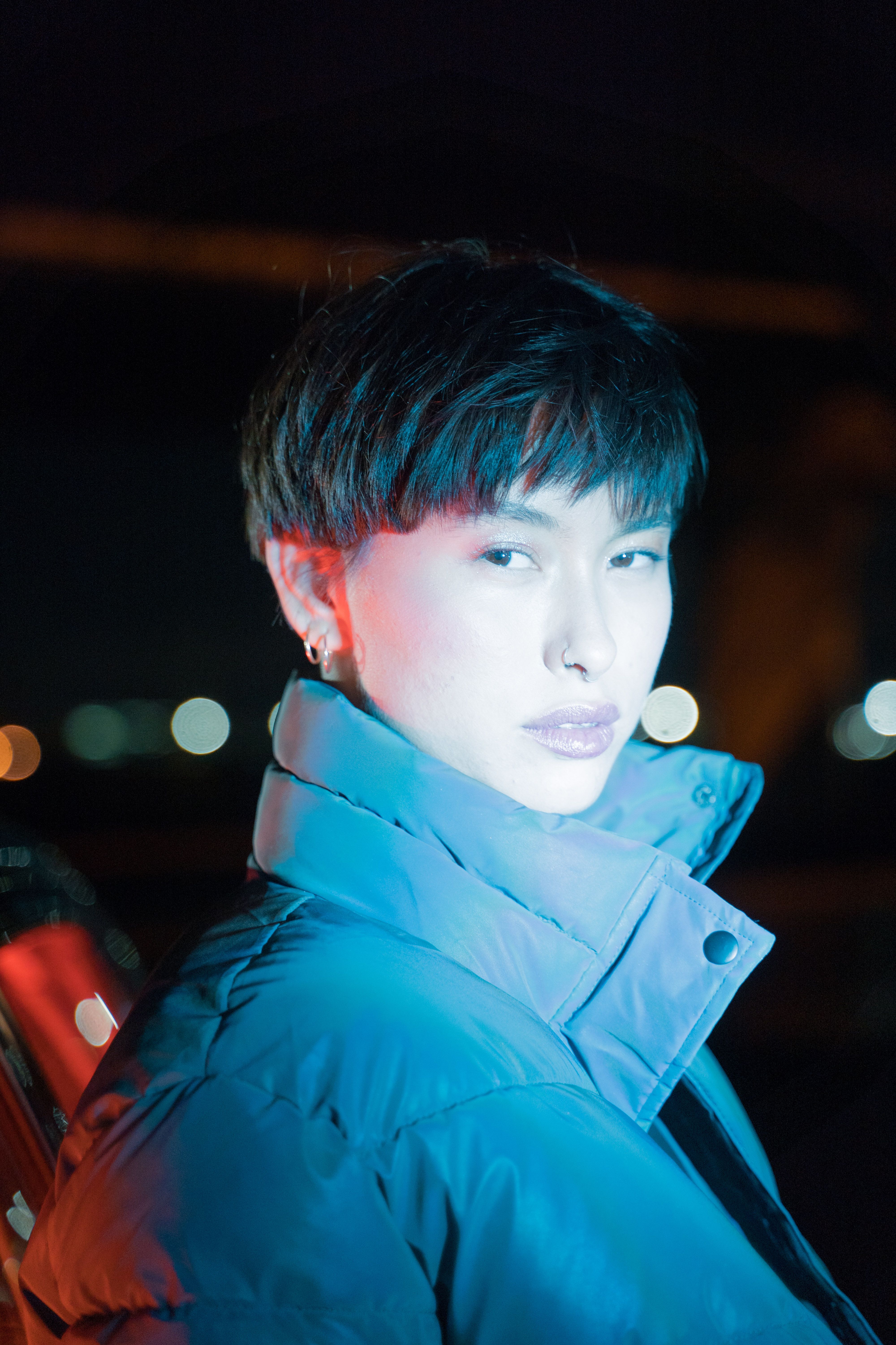 Portrait of a fashionable Asian woman with short dark hair, illuminated by vibrant city lights at ni