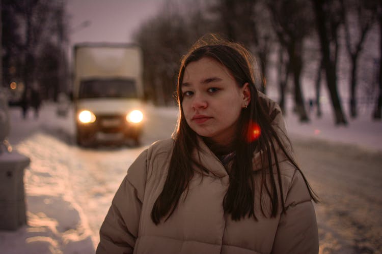 A Woman Wearing Jacket Standing On The Snow Covered Road Backlit By The Truck Headlights