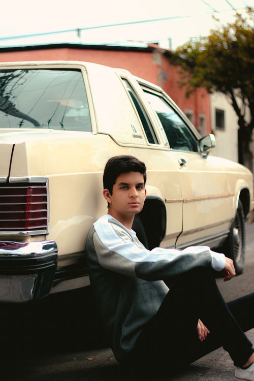 Free A young man sits casually against a classic car outdoors Stock Photo