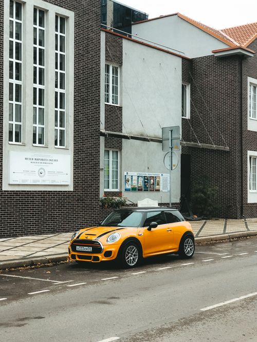 Free Yellow Mini Cooper parked on street in front of brick building in Kaliningrad, Russia. Urban transportation scene. Stock Photo