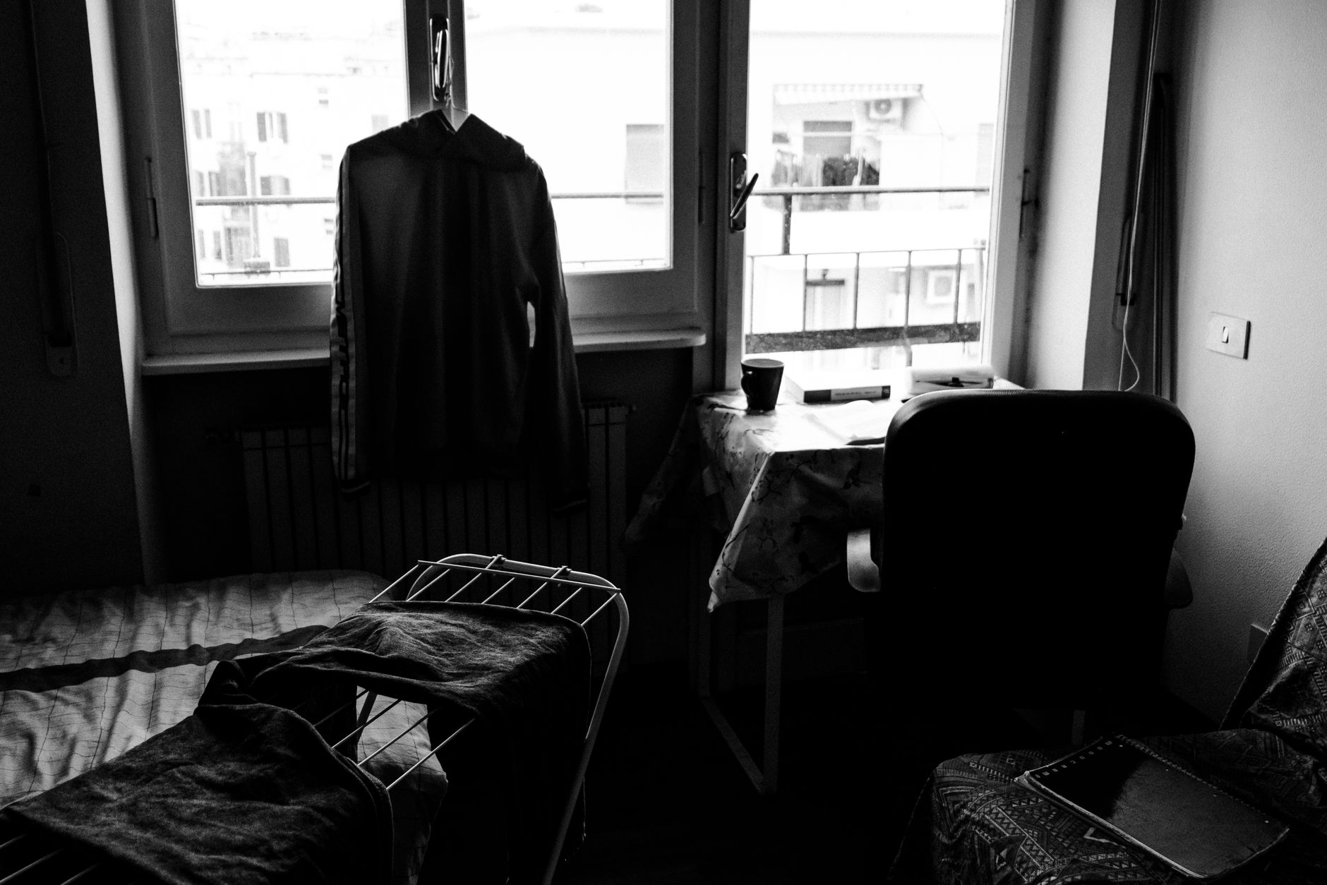 A black and white photo of a room in Rome, featuring a window view, drying laundry, and a cluttered desk.