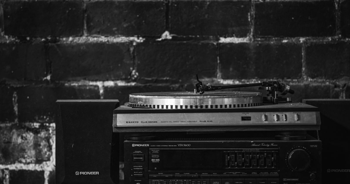 Monochrome image of a vintage turntable and audio setup with speakers against a brick wall.