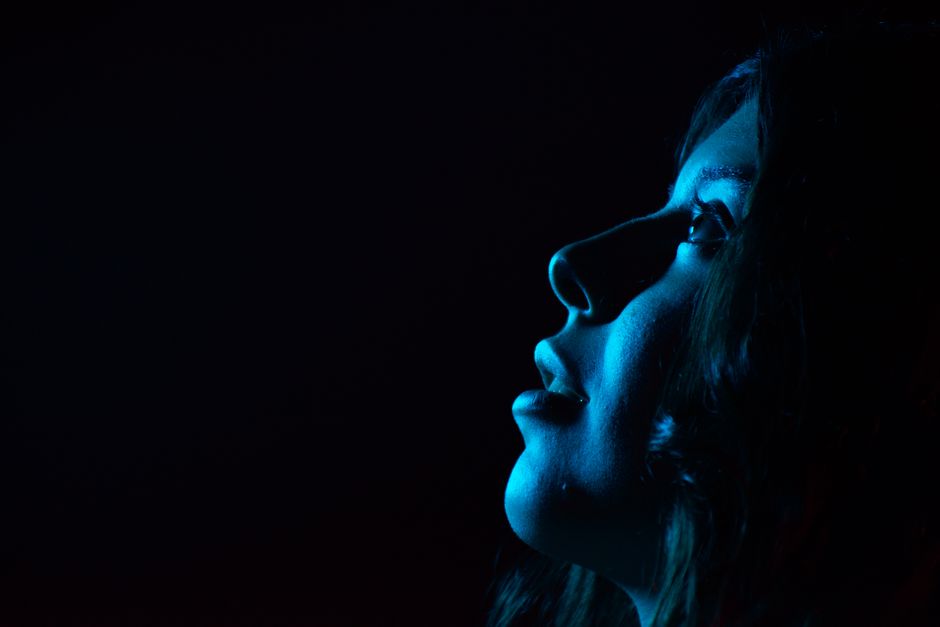 A striking portrait of a woman's side profile illuminated by blue light, creating a moody atmosphere.