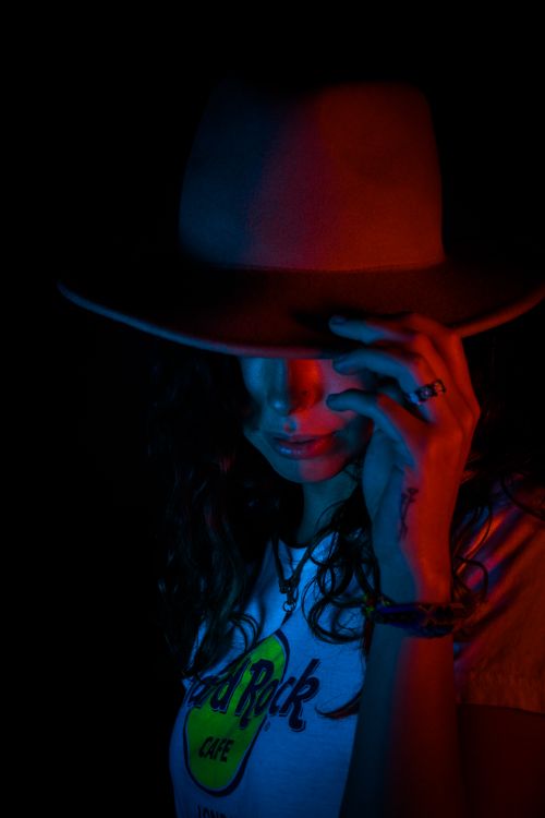 Free A woman in a hat with neon lighting creates a mysterious fashion scene. Stock Photo
