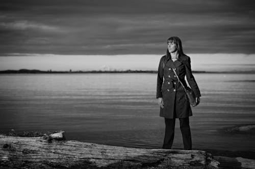 Free Grayscale Photo of Woman in Coat Standing on Wooden Dock Stock Photo