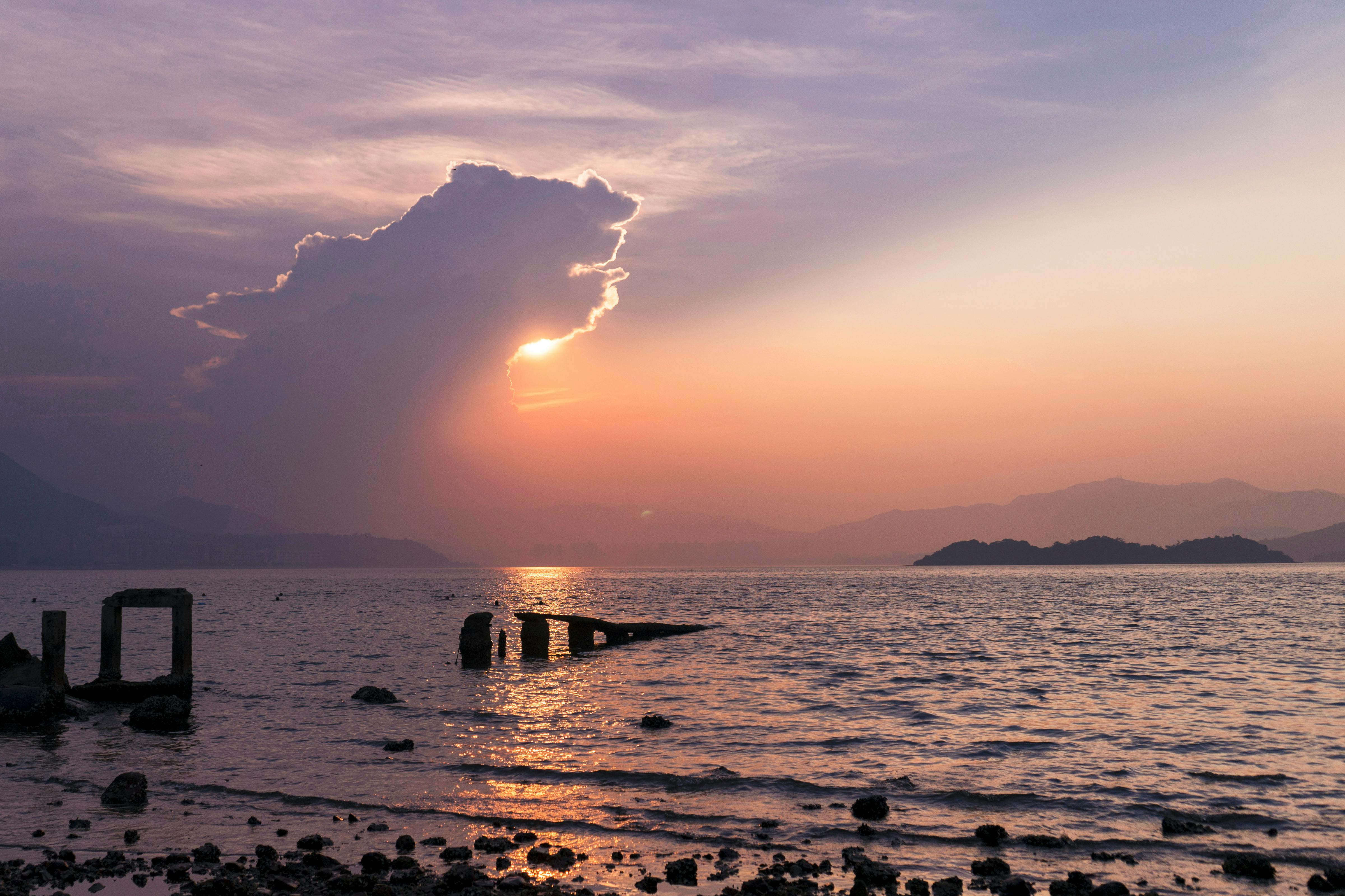 Tranquil sunset view over Hong Kong seashore with orange hues and distant mountains.