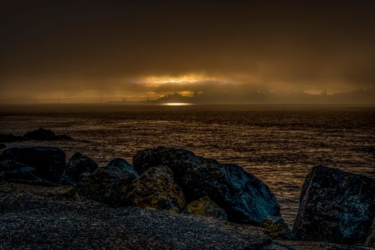 A dramatic sunset casts a silhouette over a rocky seascape with an overcast sky.