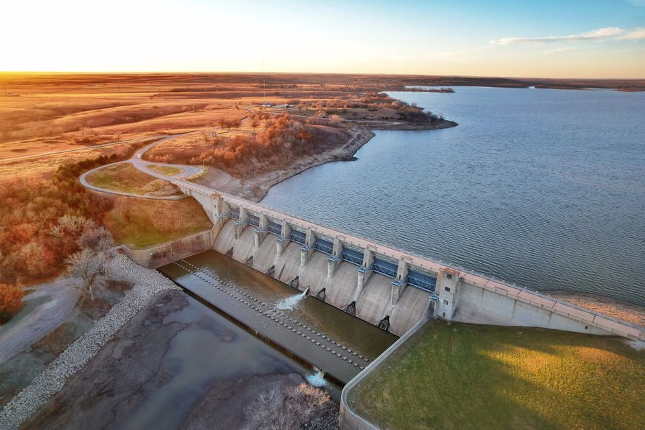 Photo by Taylor Hunt A scenic aerial view of a dam in Kansas, USA, at sunset with expansive lake and landscape.