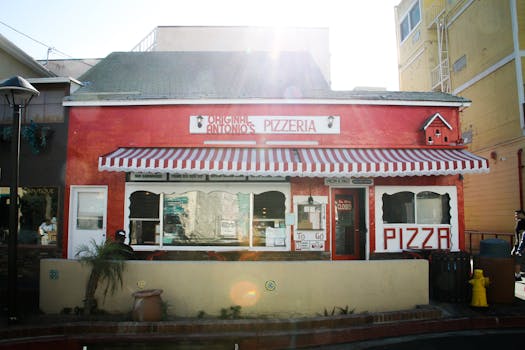 Exterior of Original Antonio's Pizzeria with red facade and striped awning under bright sunlight.