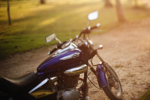 Free Close-up of a polished motorcycle parked on a sunlit dirt road with green field background. Stock Photo