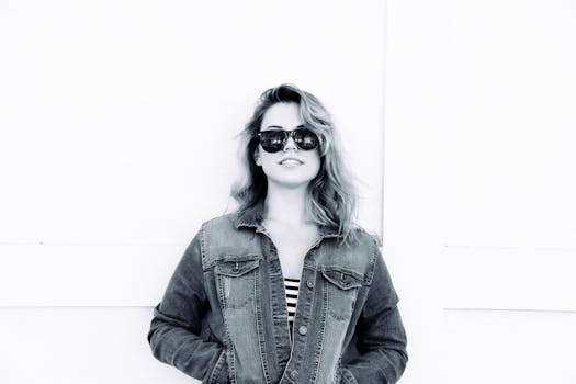 一位身着牛仔夹克、戴着太阳镜的年轻女子，在单色肖像中散发着风格与自信