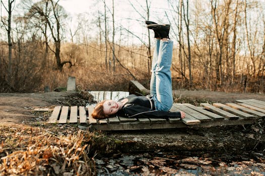 Young woman in casual attire lying on wooden bridge with legs up in a serene forest setting.
