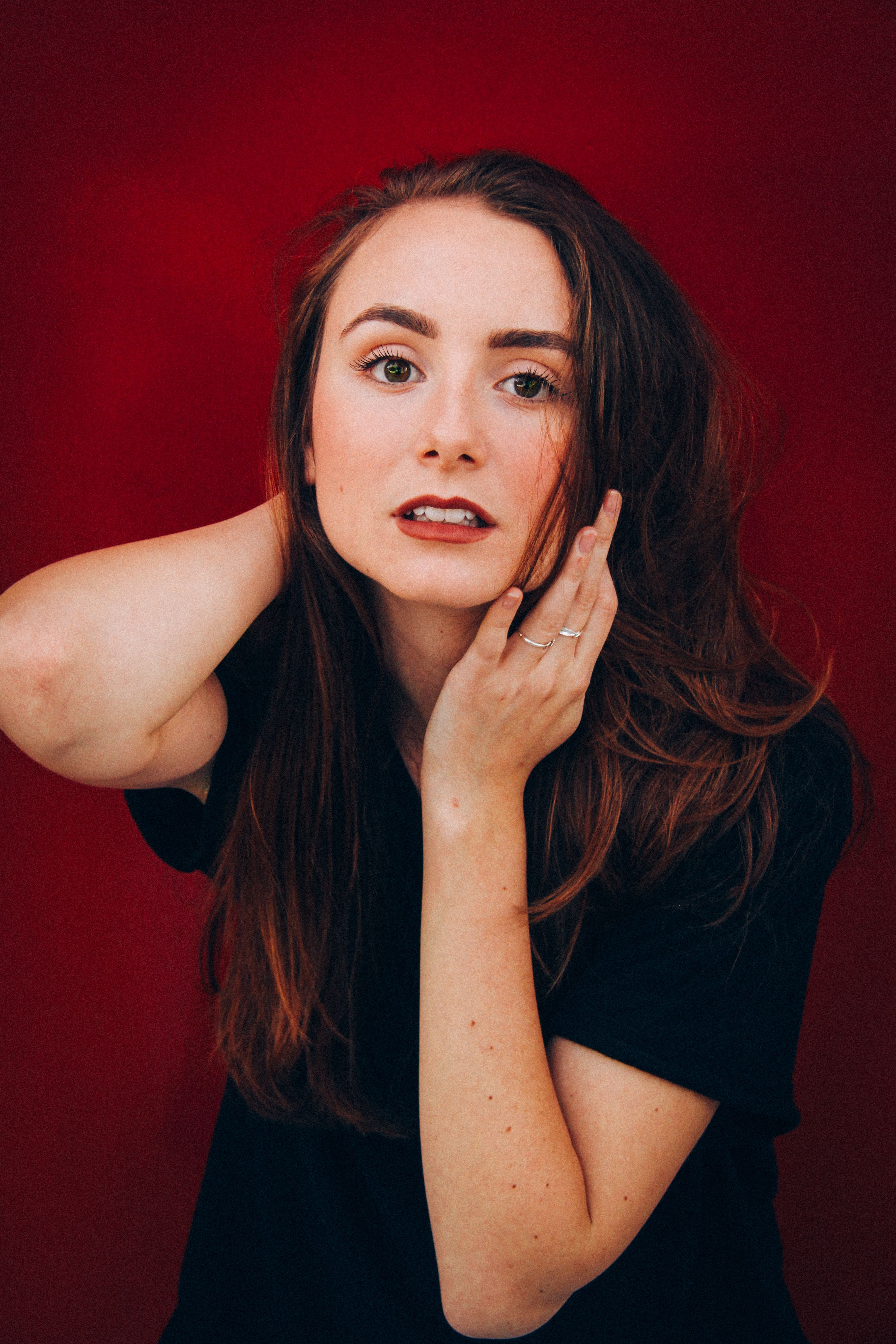 Captivating portrait of a young woman with striking features against a red backdrop, exuding glamour and style.