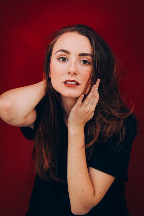 Free Captivating portrait of a young woman with striking features against a red backdrop, exuding glamour and style. Stock Photo