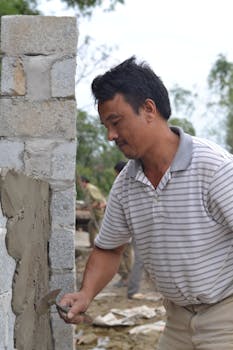 Asian man applying cement to a brick wall on a construction site. Outdoor work setting.