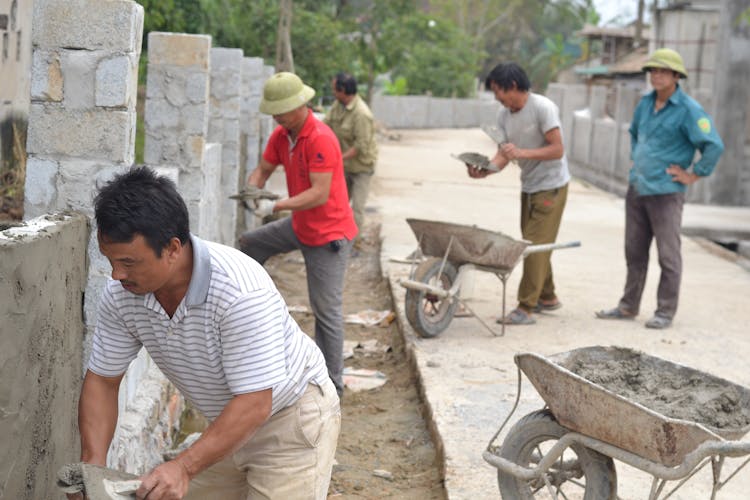 A Group Of Construction Workers Applying Cement On Wall