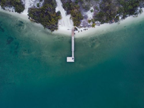 Free Stunning aerial shot of a dock extending into calm, turquoise sea from a lush, wooded island shore. Stock Photo