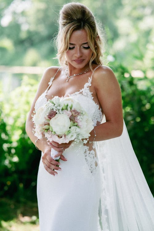 A Woman in White Spaghetti Strap Wedding Dress Holding Flower Bouquet