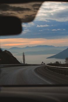 View of a winding road and mountains through a car windshield at twilight, capturing a serene travel moment.