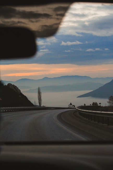 View of a winding road and mountains through a car windshield at twilight, capturing a serene travel moment.