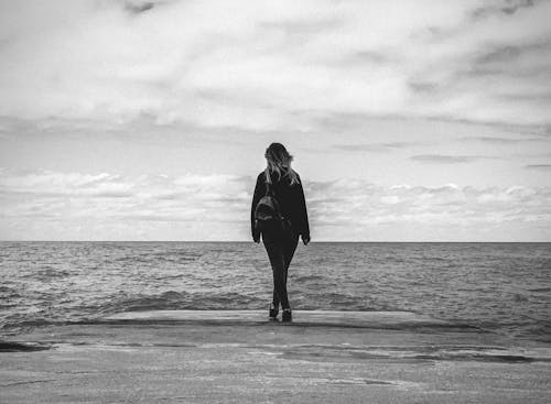 Free Woman in Black Coat Standing on Beach Stock Photo